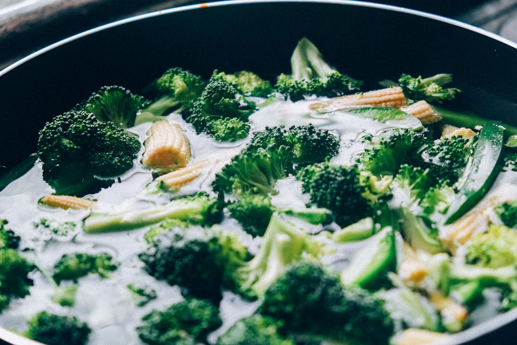 Close-up of fresh broccoli and baby corn sizzling in a pan for a healthy meal.