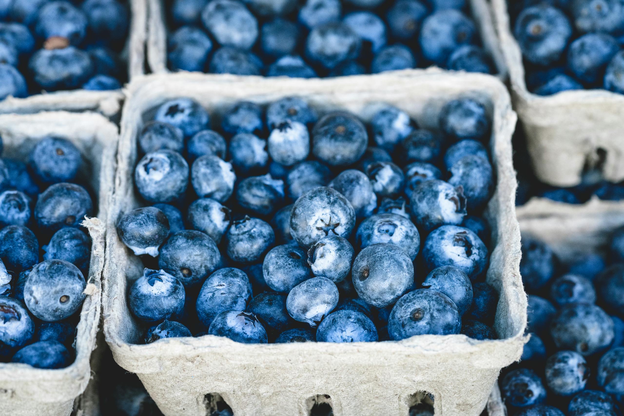 Close-up of fresh organic blueberries in cardboard trays at a market, showcasing their vibrant blue color and ripe appearance.